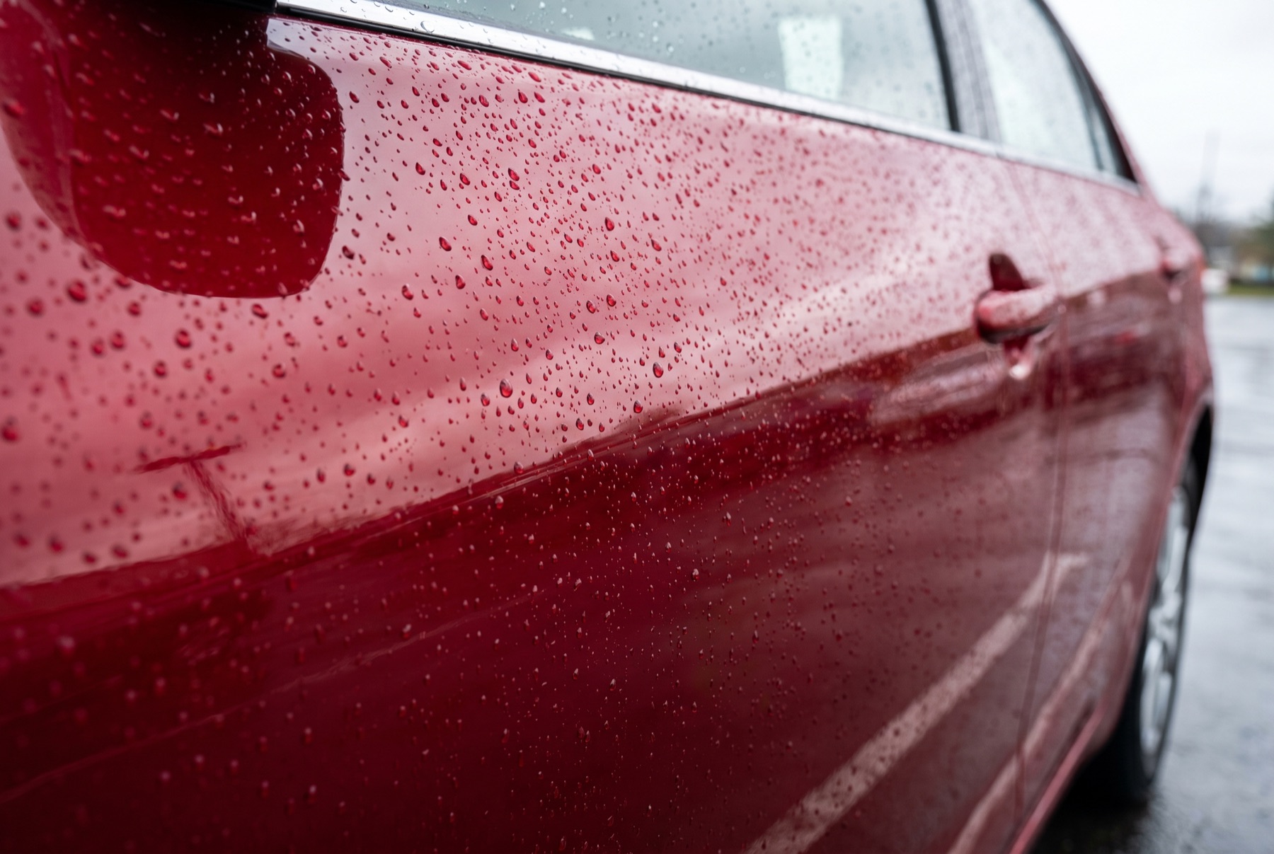 Water beading on the ceramic-coated door of a red saloon