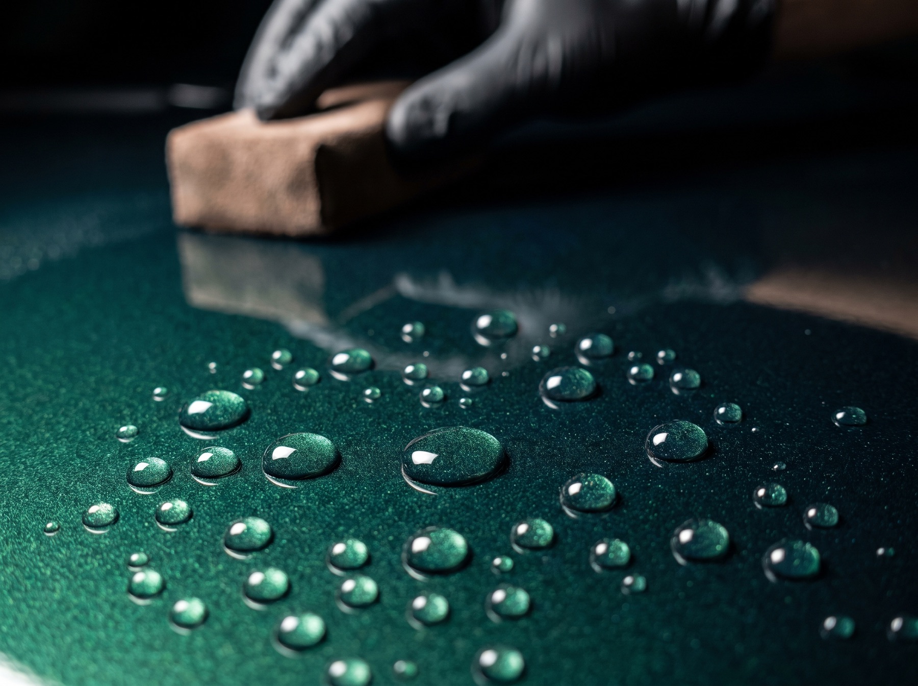 Water beading on freshly ceramic-coated green metallic paint with an applicator in the background